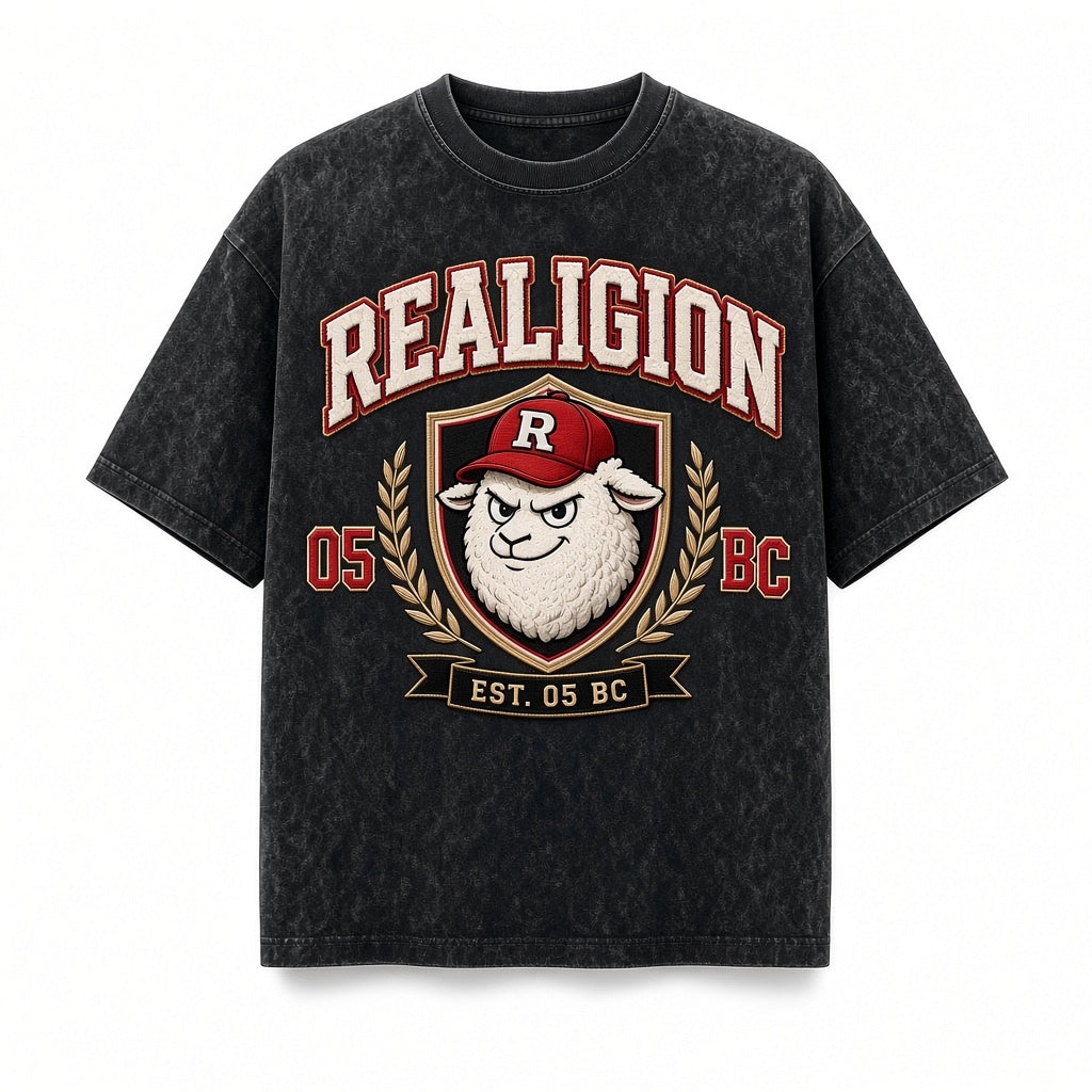 Vintage-wash black REALIGION Varsity Crest Tee with cream arched lettering, lamb mascot in a red R cap inside a gold-trimmed shield with laurels, and Est. 05 BC banner